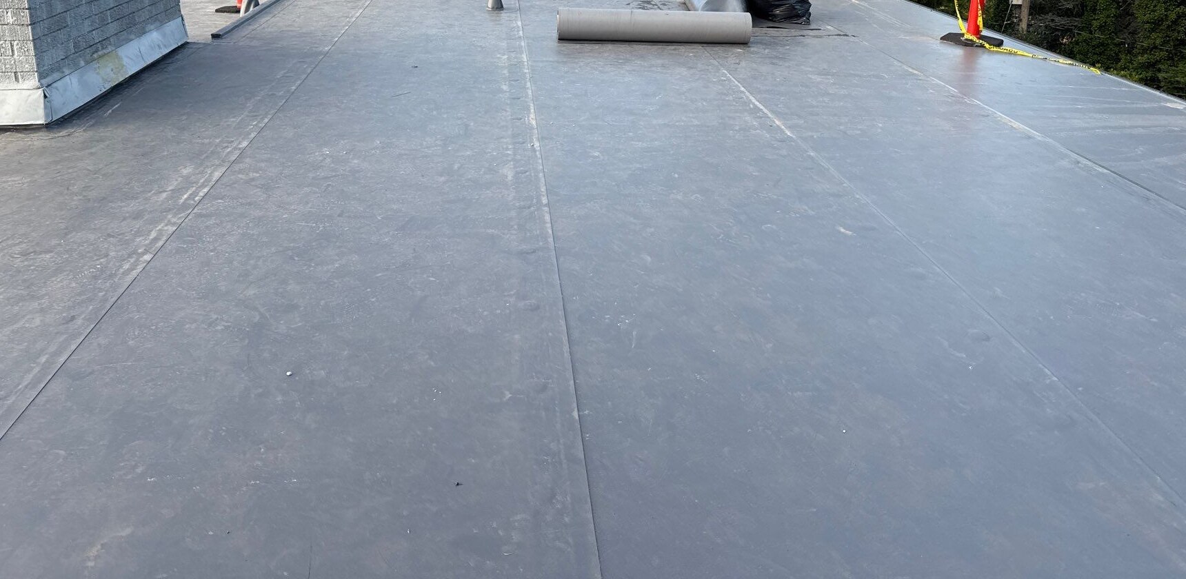 Broad gray roof surface with visible seams, a masonry chimney and a material roll