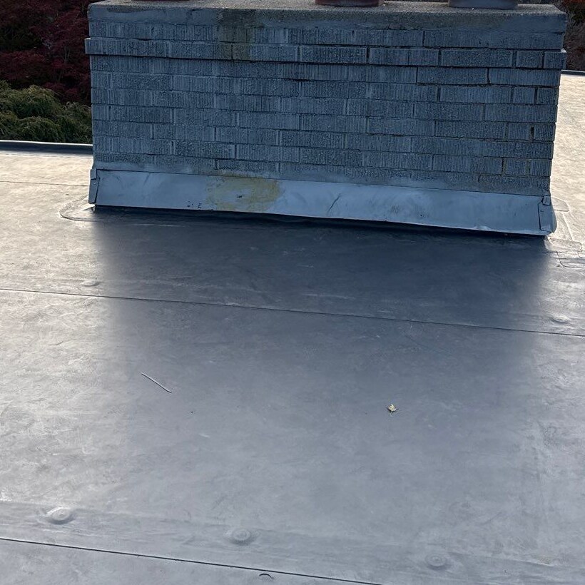 Masonry chimney with metal detailing at its base adjoining the gray roof surface