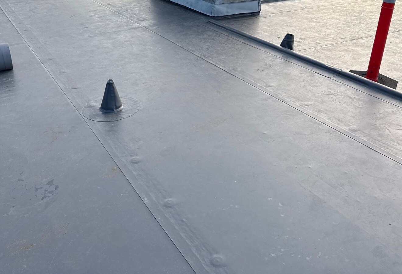 Gray roof field with visible seams, raised roof penetrations and a chimney base