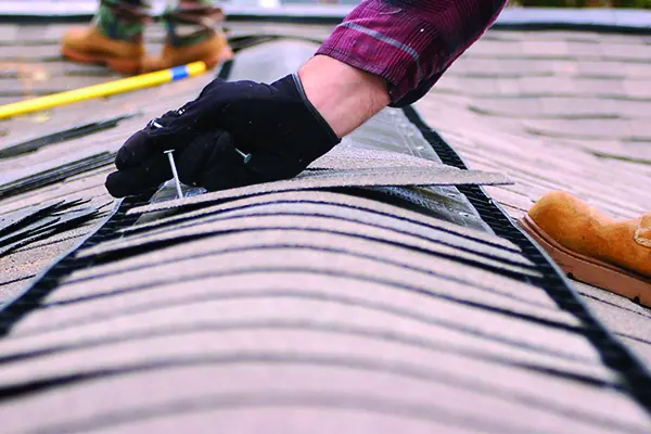 Roofer hand-nailing a replacement composition shingle into a repaired section of roof
